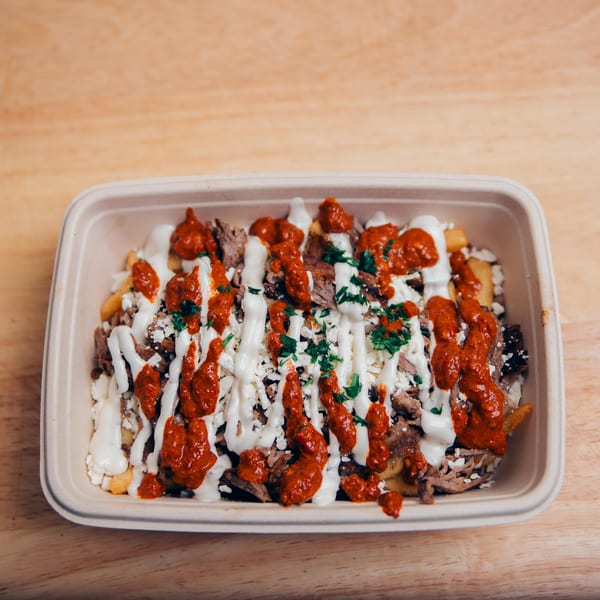 Jarasa Kabob's loaded fries with meat, white sauce, red sauce, and parsley in a to-go container.