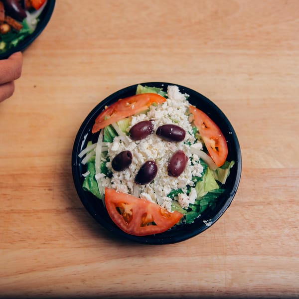 A Jarasa Kabob side salad with lettuce, tomatoes, feta cheese, and olives on a wooden table.