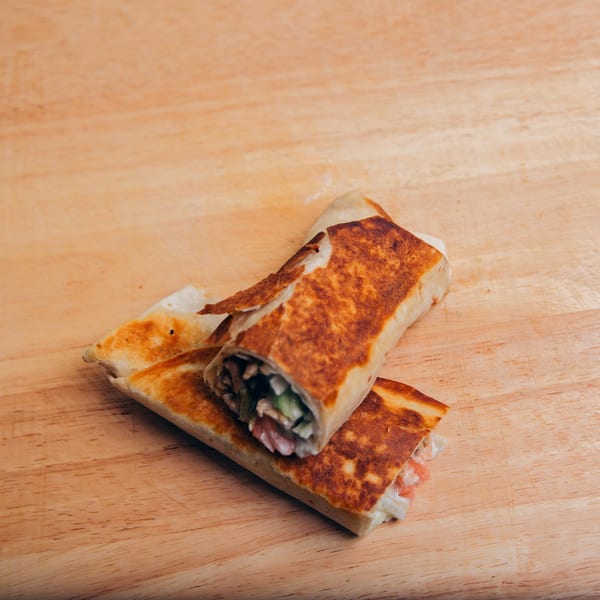 Two golden-brown Jarasa Kabob wraps, filled with meat and vegetables, rest on a wooden surface.