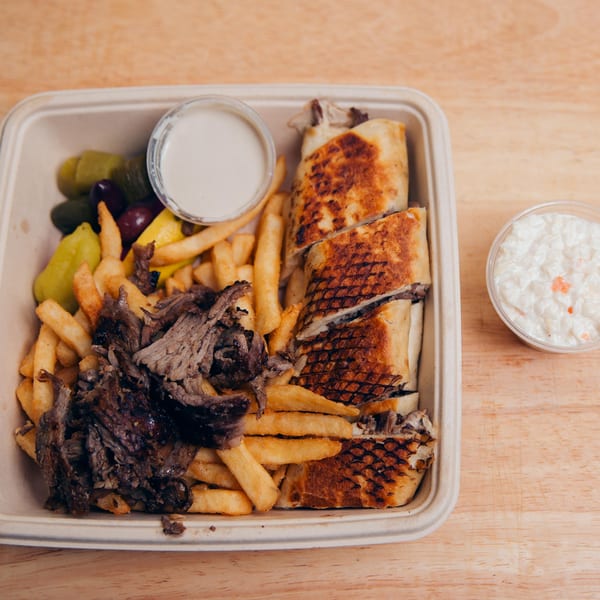Jarasa Kabob's shawarma plate with sliced meat, fries, pickles, olives, and two sauces.
